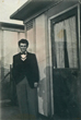 Brian standing outside back door of the prefab wearing blue trousers green jacket pink shirt and a black bow tie