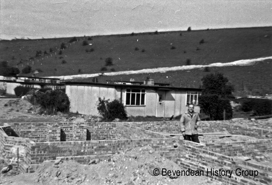 Len Feast standing onside low walls of bungalow